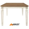 Η τραπεζαρία Realyn, της Ashley, με  επεκτεινόμενο τραπέζι και έξι καρέκλες, έχει χρώμα σε παλαιωμένο λευκό. Οι καρέκλες έχουν κορδελωτό σχέδιο στην πλάτη.